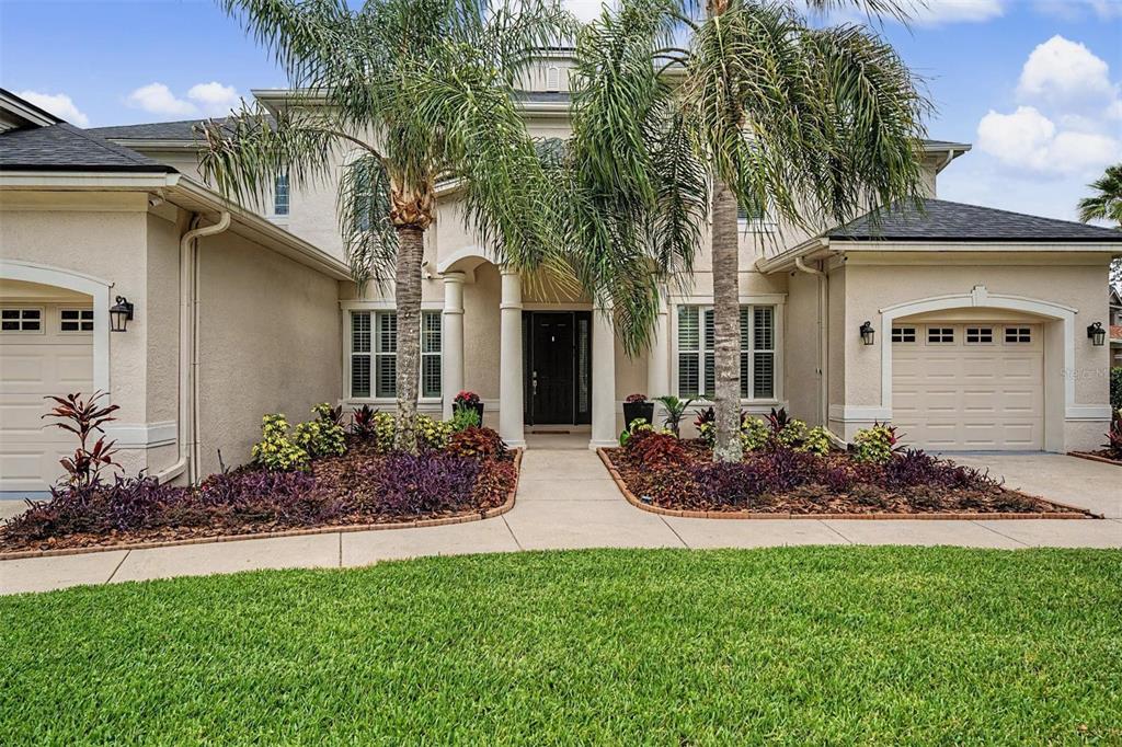 A two-story house with a beige stucco exterior, two garages, and palm trees in front — 5116 ABISHER WOOD LANE, BRANDON, FL