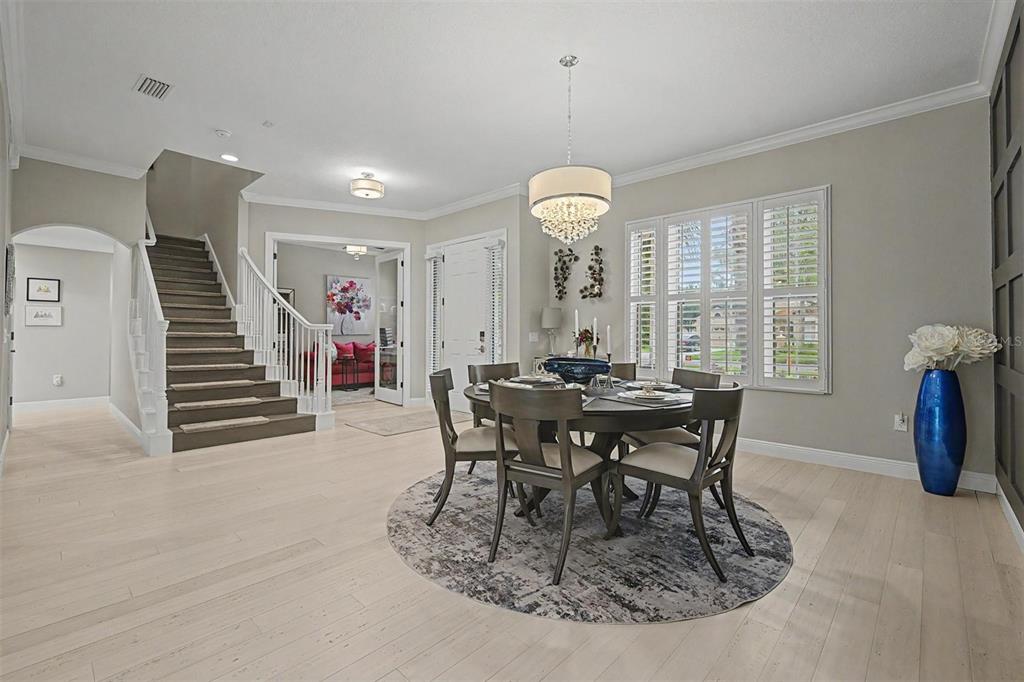 A dining area features a round table, chandelier, and staircase on light wood flooring — 5116 ABISHER WOOD LANE, BRANDON, FL