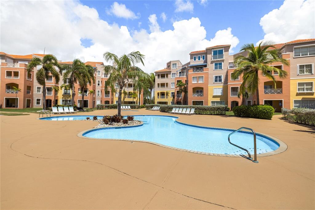A swimming pool sits in the courtyard of a multi-story apartment complex with palm trees — . CANDELERO DRIVE UNIT A303, HUMACAO, PR