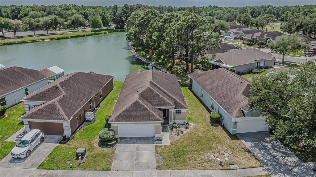An aerial view shows three suburban houses with brown roofs situated near a small lake — 5553 GALLANT FOX COURT, WESLEY CHAPEL, FL