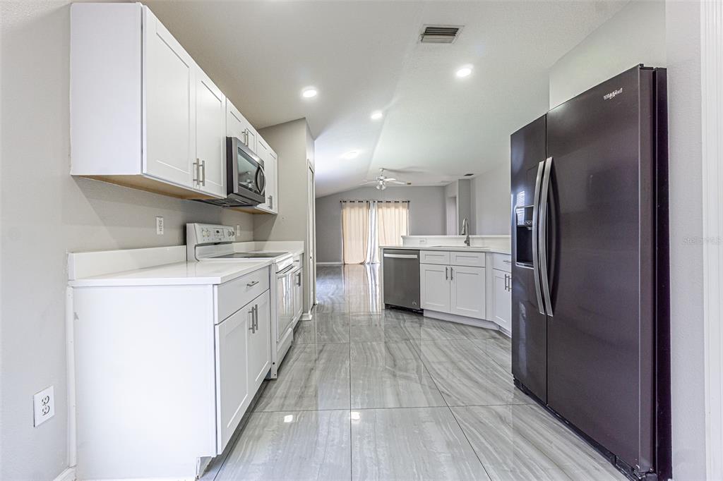 A kitchen with white cabinets, stainless steel appliances, and gray marble-look tile flooring — 5553 GALLANT FOX COURT, WESLEY CHAPEL, FL