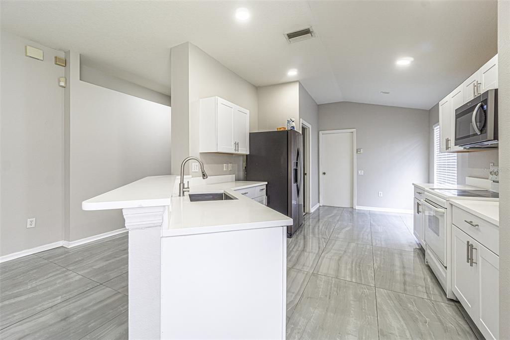 A kitchen features white cabinets, a breakfast bar with a sink, and gray tile flooring — 5553 GALLANT FOX COURT, WESLEY CHAPEL, FL