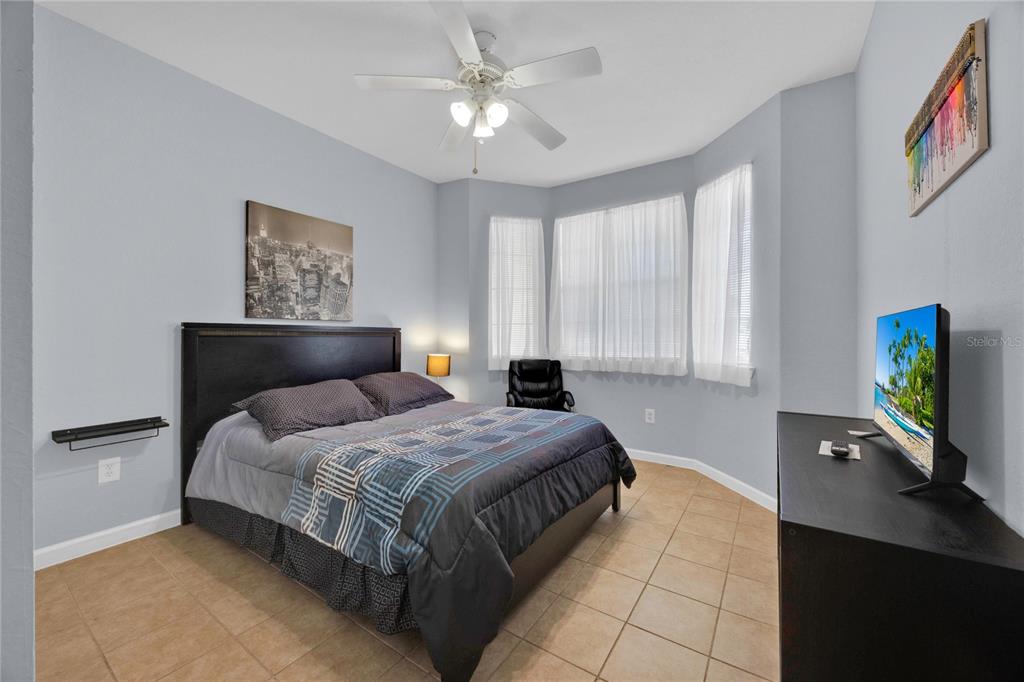 A bedroom with tile flooring, a dark bed frame, a ceiling fan, and bay windows — 804 TERRACE RIDGE CIRCLE UNIT 804, DAVENPORT, FL