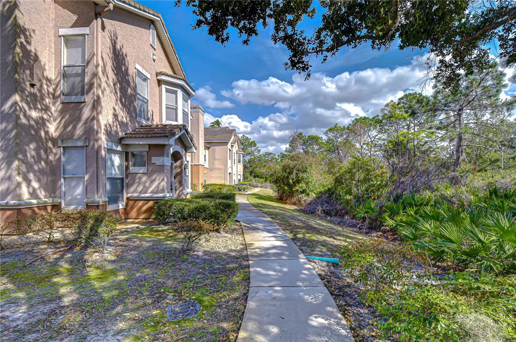 A concrete walkway leads past the side of a multi-story tan stucco apartment building — 10409 VILLA VIEW CIRCLE UNIT 10409, TAMPA, FL