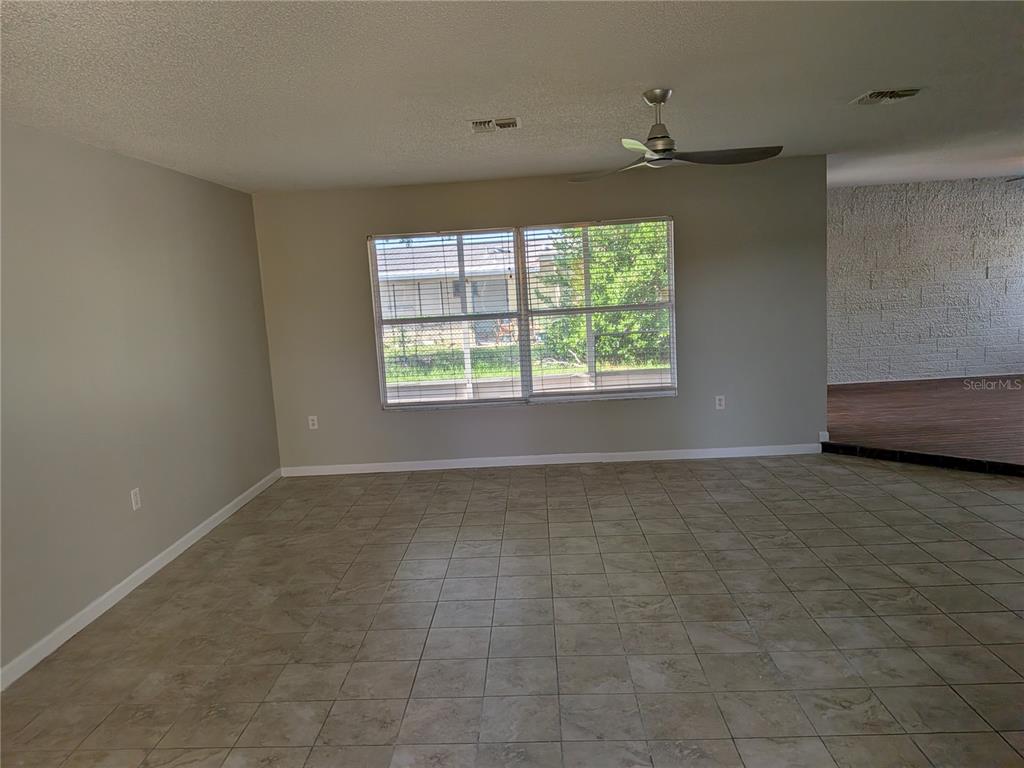 A spacious room features light-colored tile flooring, beige walls, a ceiling fan, and large windows — 8206 DEDHAM DRIVE, PORT RICHEY, FL