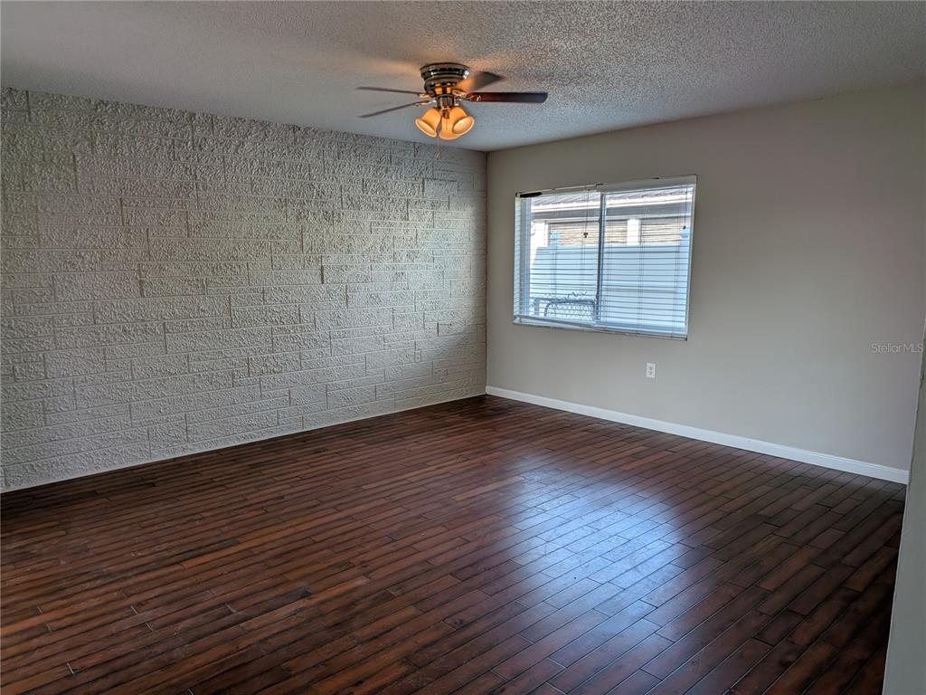An empty room features dark wood flooring, a textured brick wall, and a ceiling fan — 8206 DEDHAM DRIVE, PORT RICHEY, FL