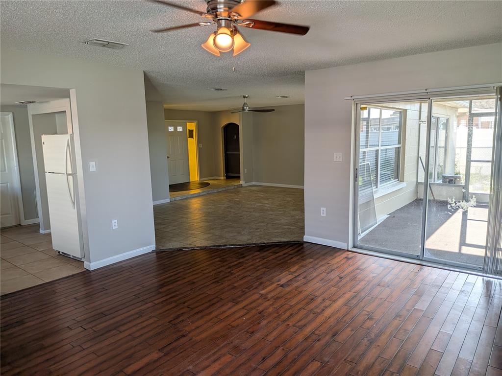 A living room with dark wood flooring, a ceiling fan, and sliding glass doors to a patio — 8206 DEDHAM DRIVE, PORT RICHEY, FL