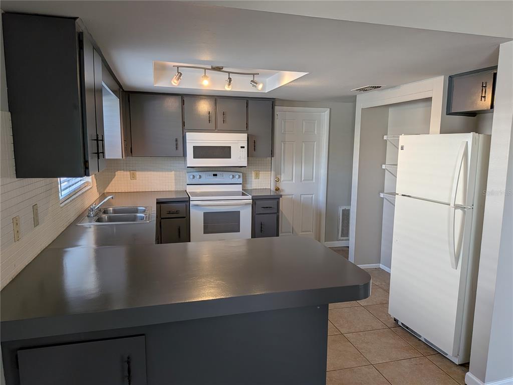 A kitchen features dark gray cabinets, a white stove, a white refrigerator, and tiled floors — 8206 DEDHAM DRIVE, PORT RICHEY, FL