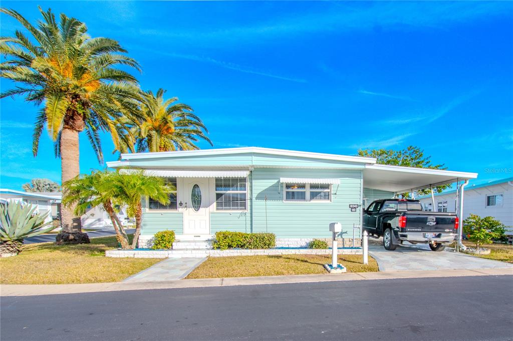 A light green manufactured home features a front porch, a carport, and palm trees — 10343 MAGNOLIA LANE UNIT 180, LARGO, FL