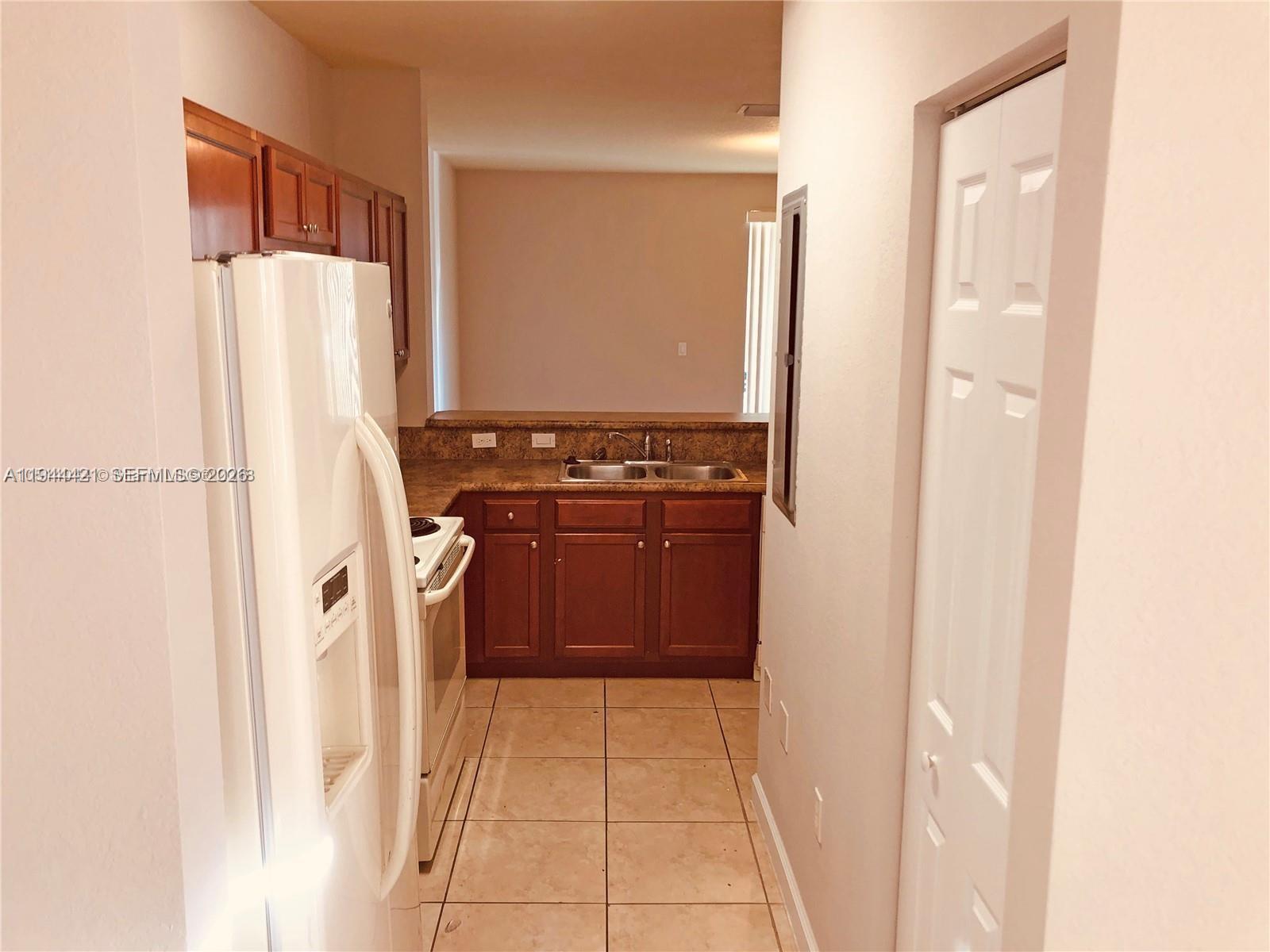 A galley kitchen features dark wood cabinets, a white refrigerator, and a double sink — 2884 SE 2 Dr # 2, Homestead FL 33033, HOMESTEAD, FL