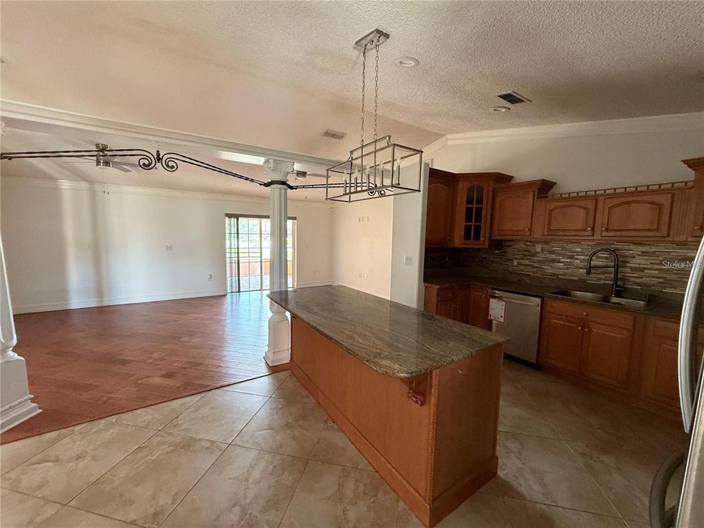 A kitchen with wood cabinets and a granite island overlooks a living area with flooring — 3900 OAK POINTE BOULEVARD, KISSIMMEE, FL