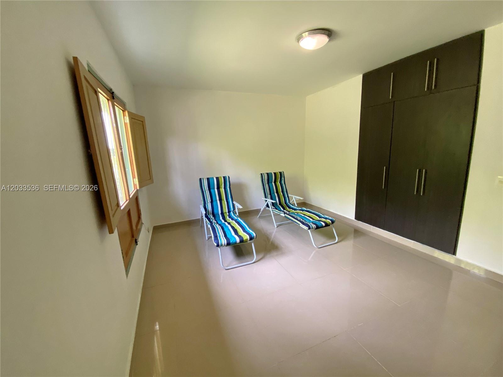 A room with light-colored tile floors, two striped lounge chairs, and dark built-in cabinets — Casa 21 Barrio Morelia, FL, FL