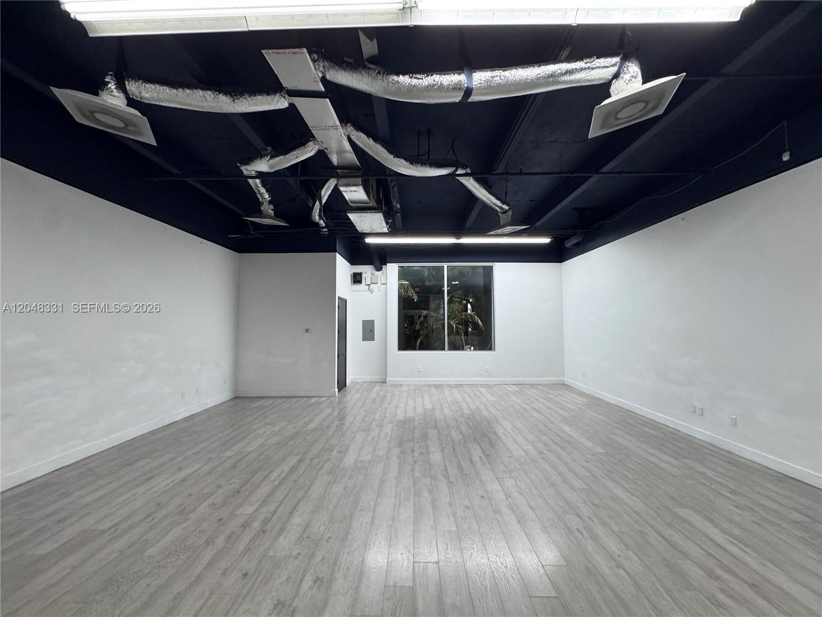 An empty commercial space features white walls, light wood-look flooring, and an exposed black ceiling — 2185 NE 163rd St, North Miami Beach FL 33162, NORTH MIAMI BEACH, FL
