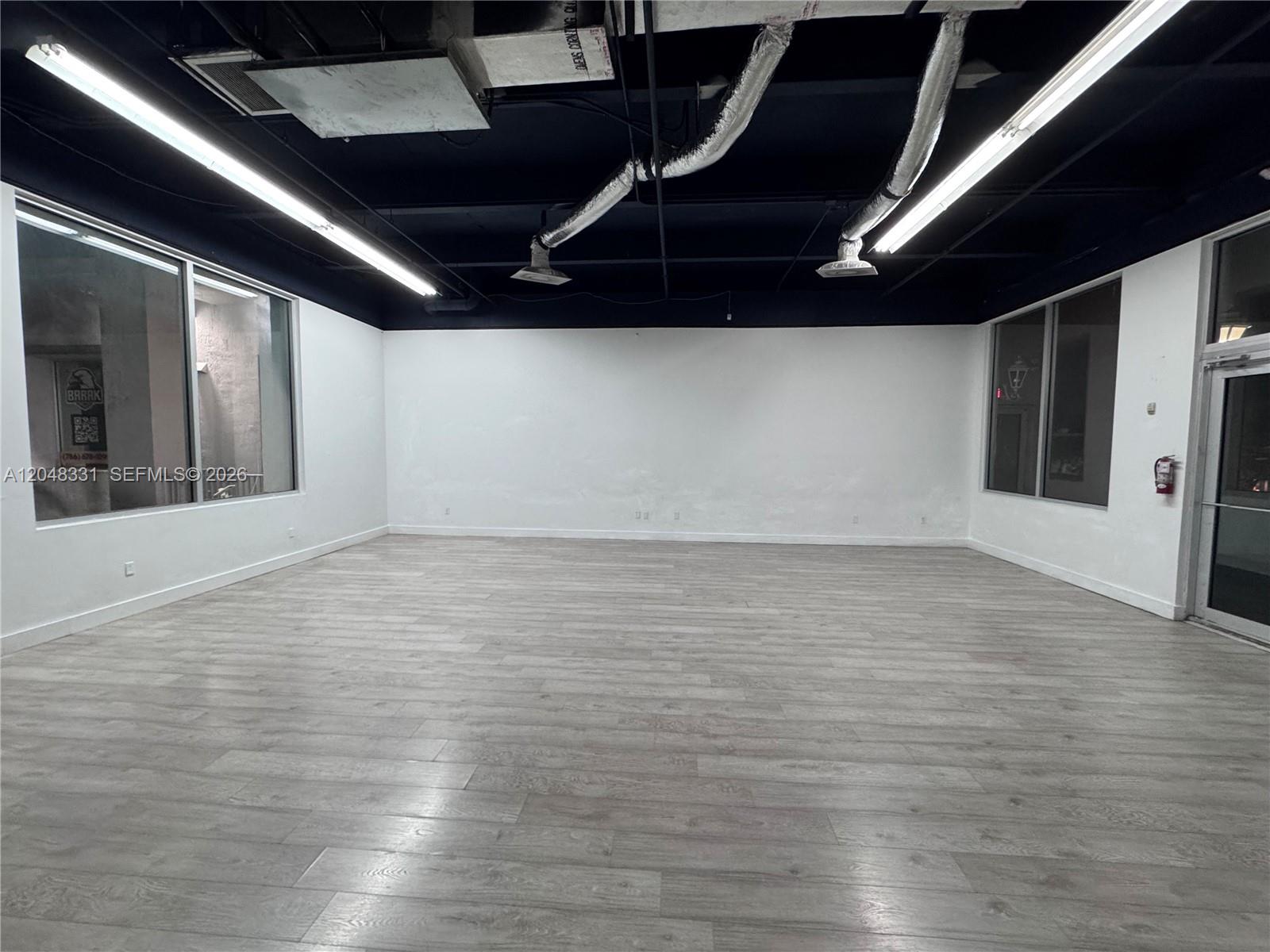 An empty commercial space features white walls, wood-look flooring, and an exposed black ceiling — 2185 NE 163rd St, North Miami Beach FL 33162, NORTH MIAMI BEACH, FL
