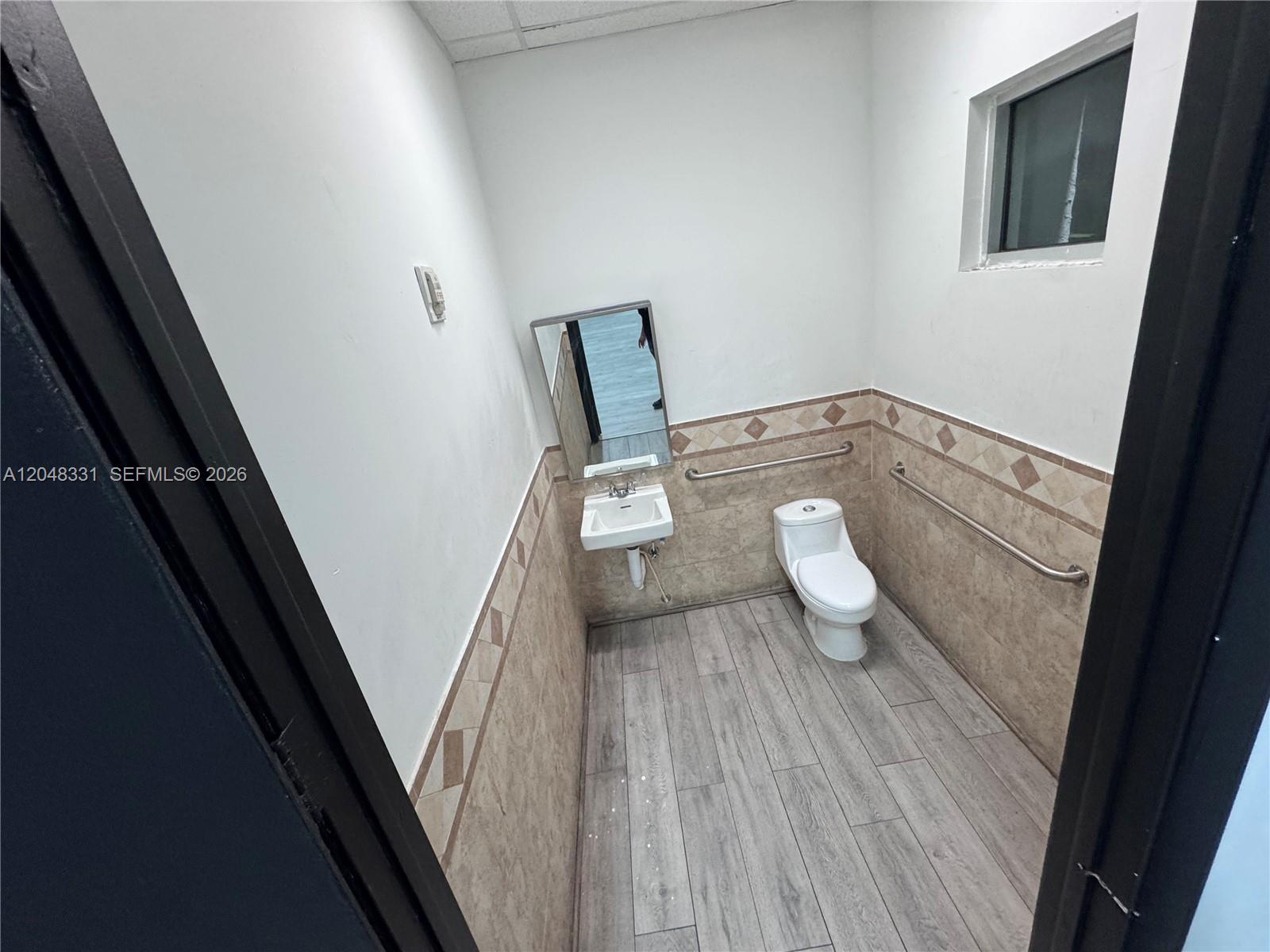 A small, accessible restroom features a wall-mounted sink, a toilet, and tiled walls — 2185 NE 163rd St, North Miami Beach FL 33162, NORTH MIAMI BEACH, FL