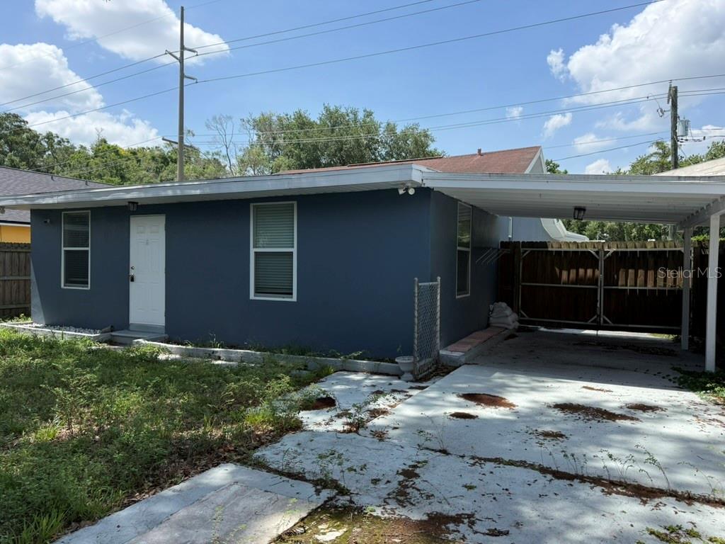 A blue single-story house features a white front door, a carport, and a concrete driveway — 1512 W KIRBY STREET, TAMPA, FL