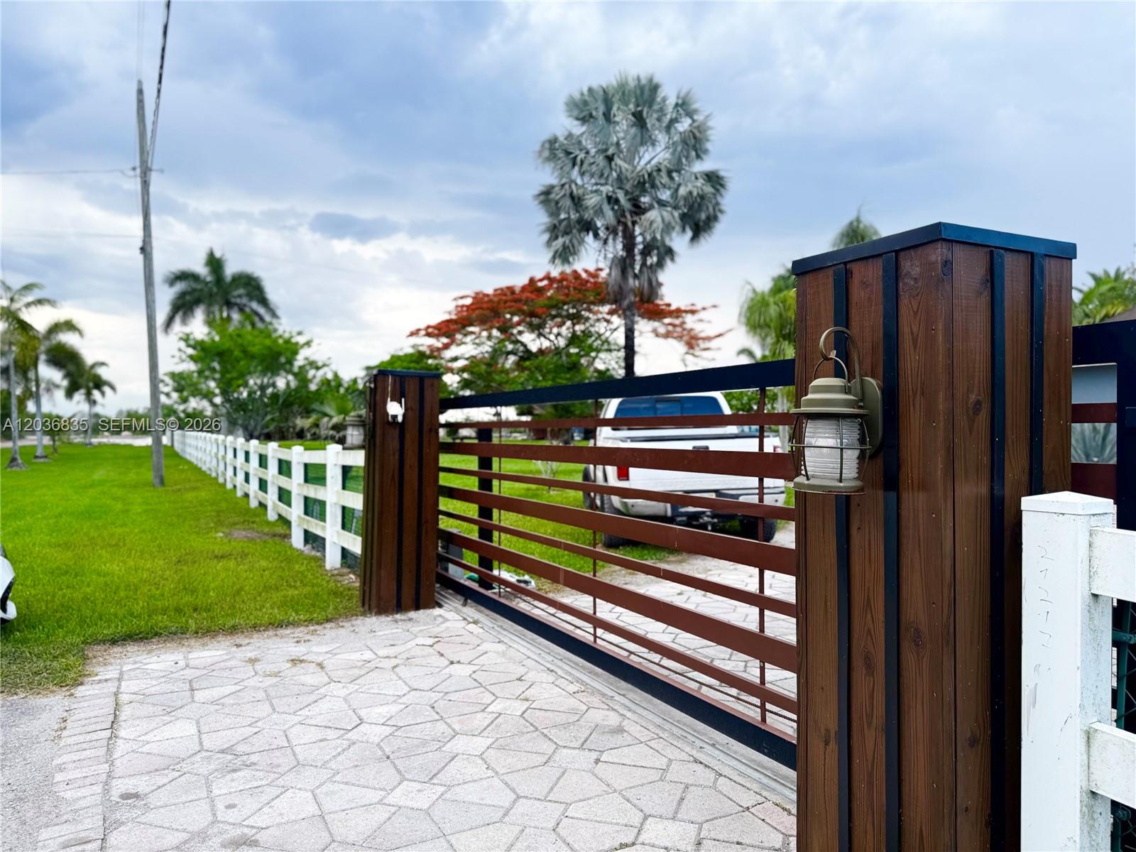 A wooden gate with horizontal slats stands at the entrance of a paved driveway — 21217 SW 160 ST, Miami FL 33187, MIAMI, FL
