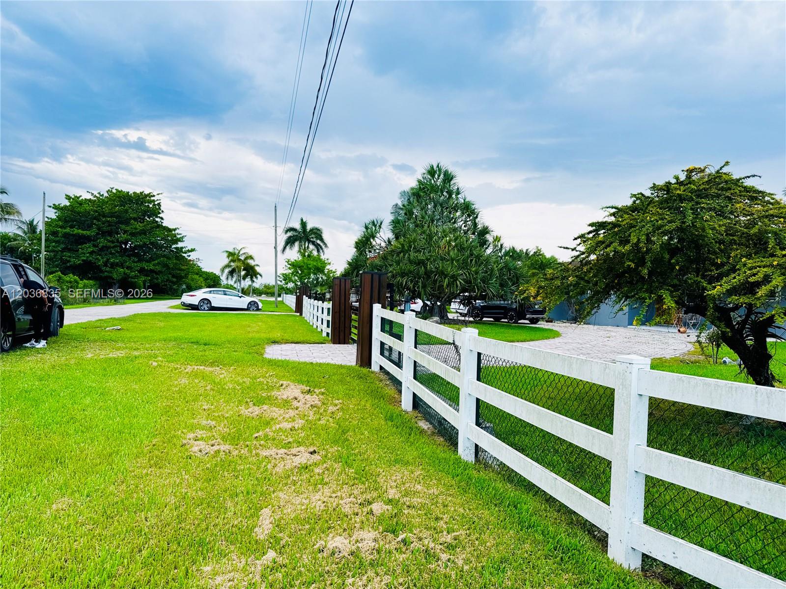 A white fence borders a grassy lawn with a paved driveway and several parked cars — 21217 SW 160 ST, Miami FL 33187, MIAMI, FL