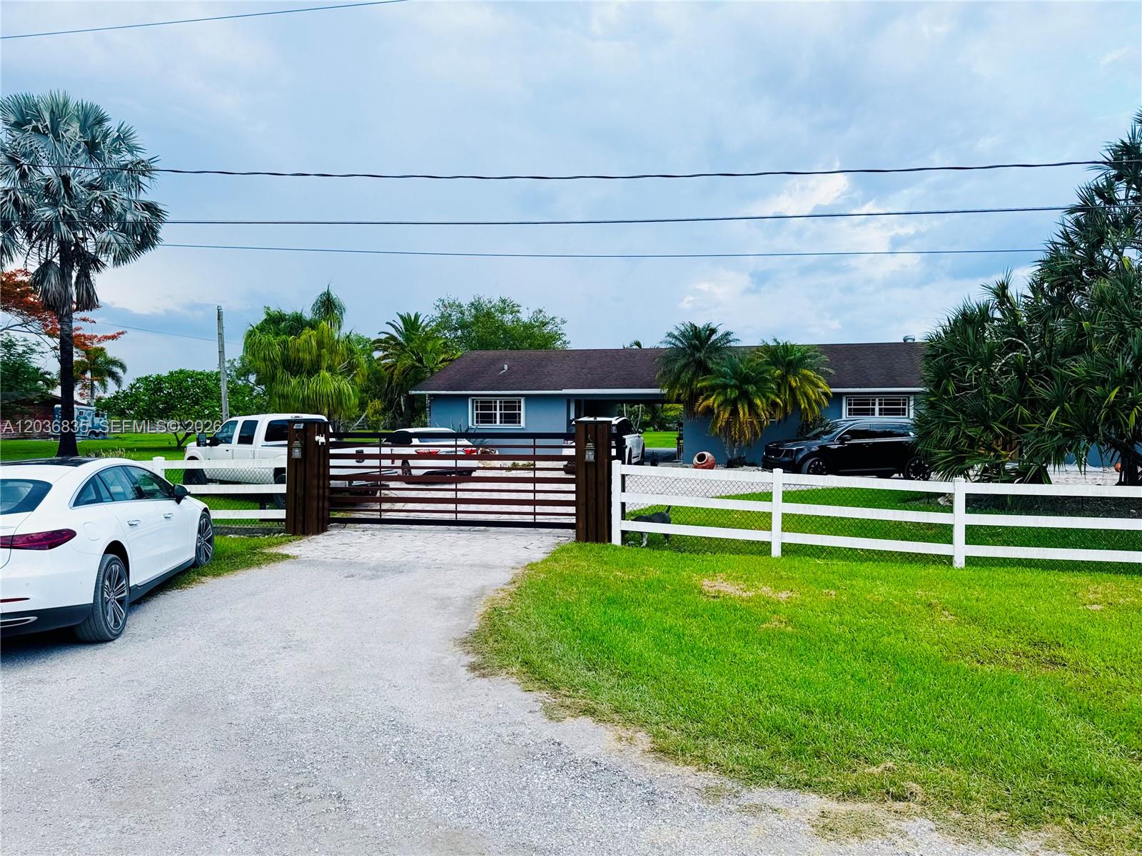 A single-story house with a gated driveway, white fence, and several parked cars — 21217 SW 160 ST, Miami FL 33187, MIAMI, FL
