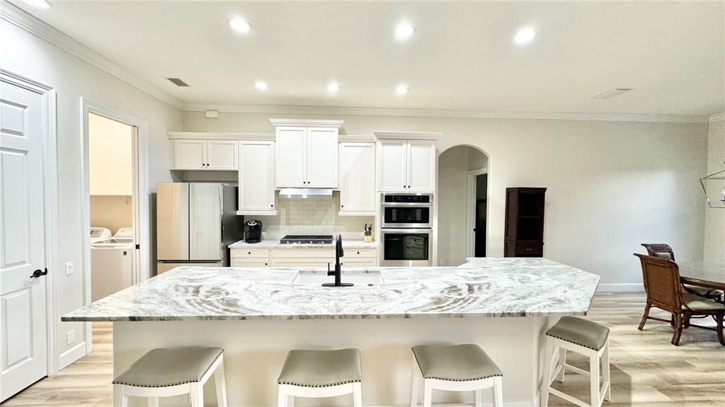 A kitchen features white cabinetry, a large marble-topped island with bar seating, and stainless appliances — 6752 SW 179TH AVENUE ROAD, DUNNELLON, FL