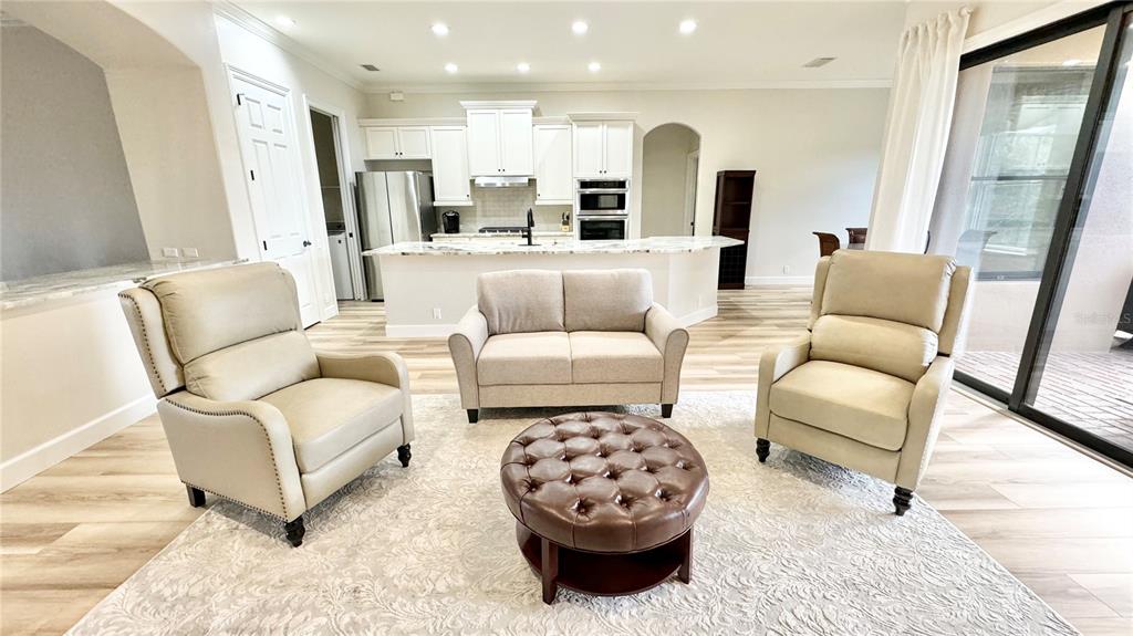 A living room with light-colored furniture, a tufted leather ottoman, and an open-concept kitchen — 6752 SW 179TH AVENUE ROAD, DUNNELLON, FL
