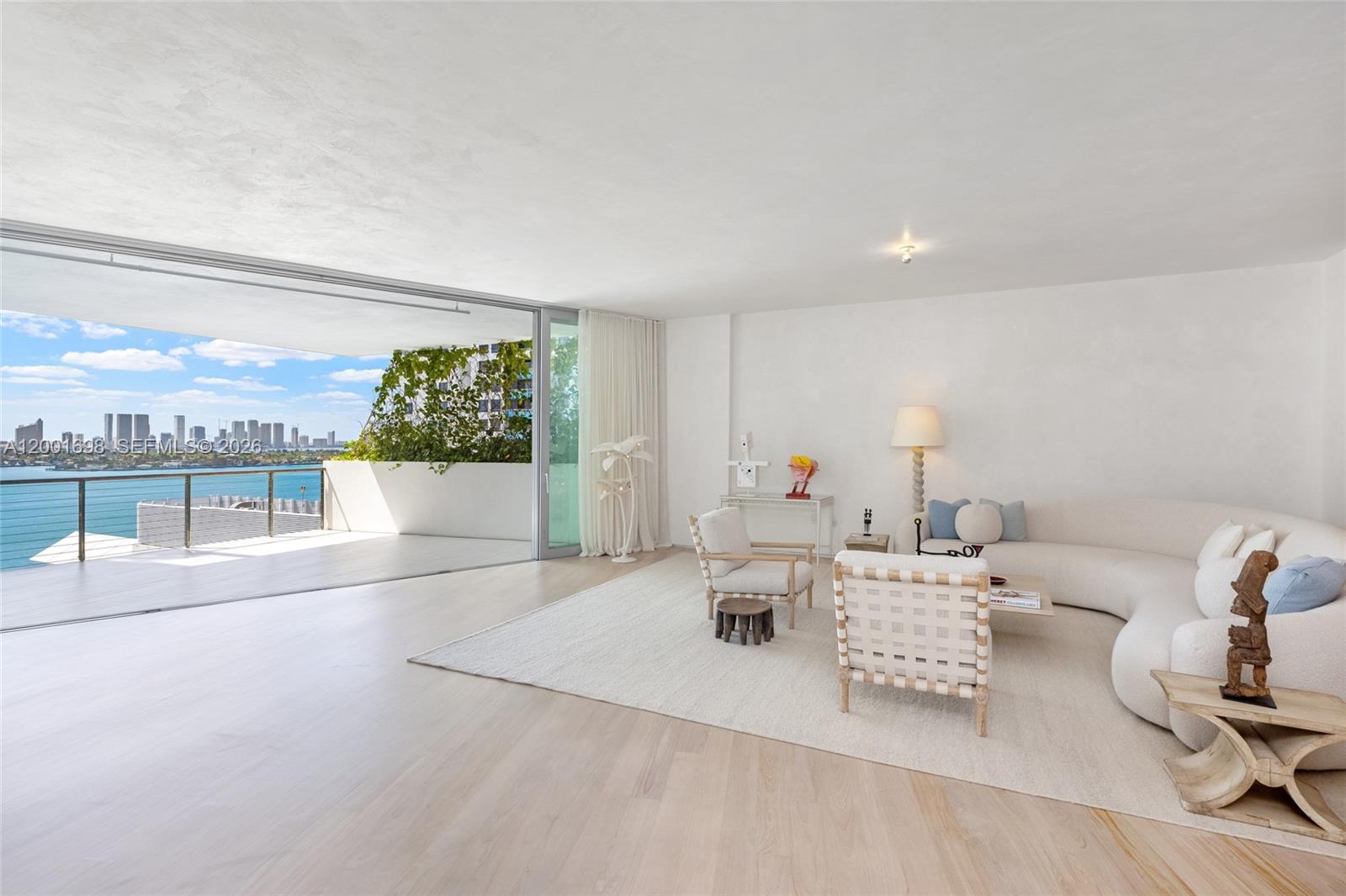 A bright living room features a curved sofa, light wood floors, and a large balcony — 1300 Monad Ter # 11E, Miami Beach FL 33139, MIAMI BEACH, FL