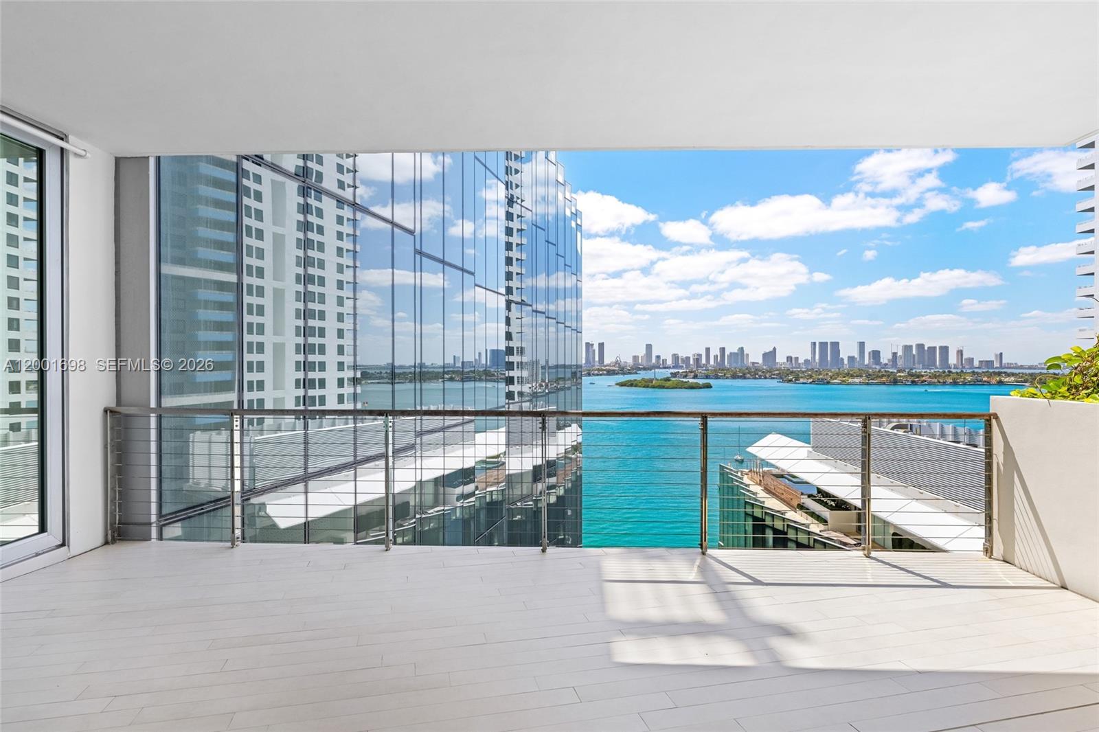 A balcony with light-colored flooring and a metal railing overlooks a bay and city skyline — 1300 Monad Ter # 11E, Miami Beach FL 33139, MIAMI BEACH, FL