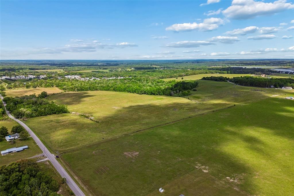 An aerial view shows a large, open grassy field bordered by a road and trees — JOHNSTON ROAD, DADE CITY, FL