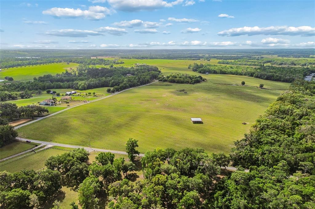 An aerial view shows a large, grassy pasture with a small shed and surrounding trees — JOHNSTON ROAD, DADE CITY, FL