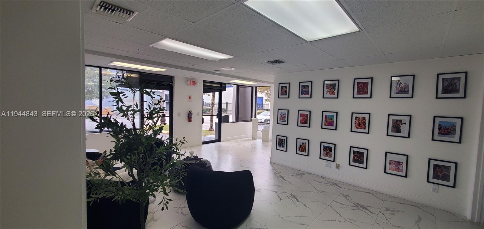 A bright office lobby features white marble-look tile floors and a gallery wall of framed photos — 2100 NW 93rd Ave, Doral FL 33172, DORAL, FL