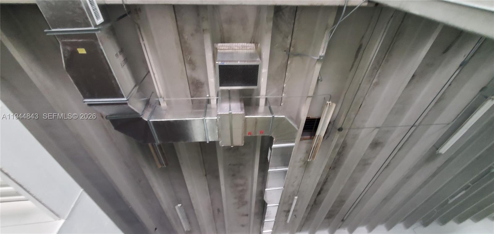 This low-angle view shows exposed metal ductwork and lighting fixtures mounted on a concrete ceiling — 2100 NW 93rd Ave, Doral FL 33172, DORAL, FL