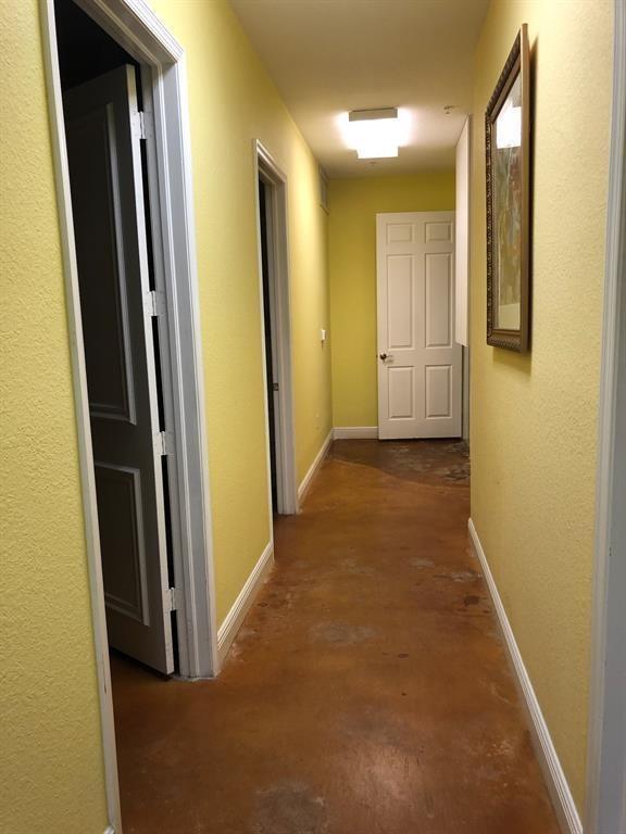 A hallway with yellow walls, white trim, and stained concrete flooring leads to a door — 6848 Griffin Road # 6, Davie FL 33314, DAVIE, FL