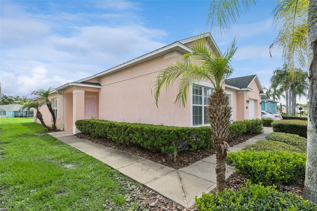 A pink stucco house with a concrete walkway, manicured hedges, and palm trees — 621 RESERVE DRIVE, DAVENPORT, FL