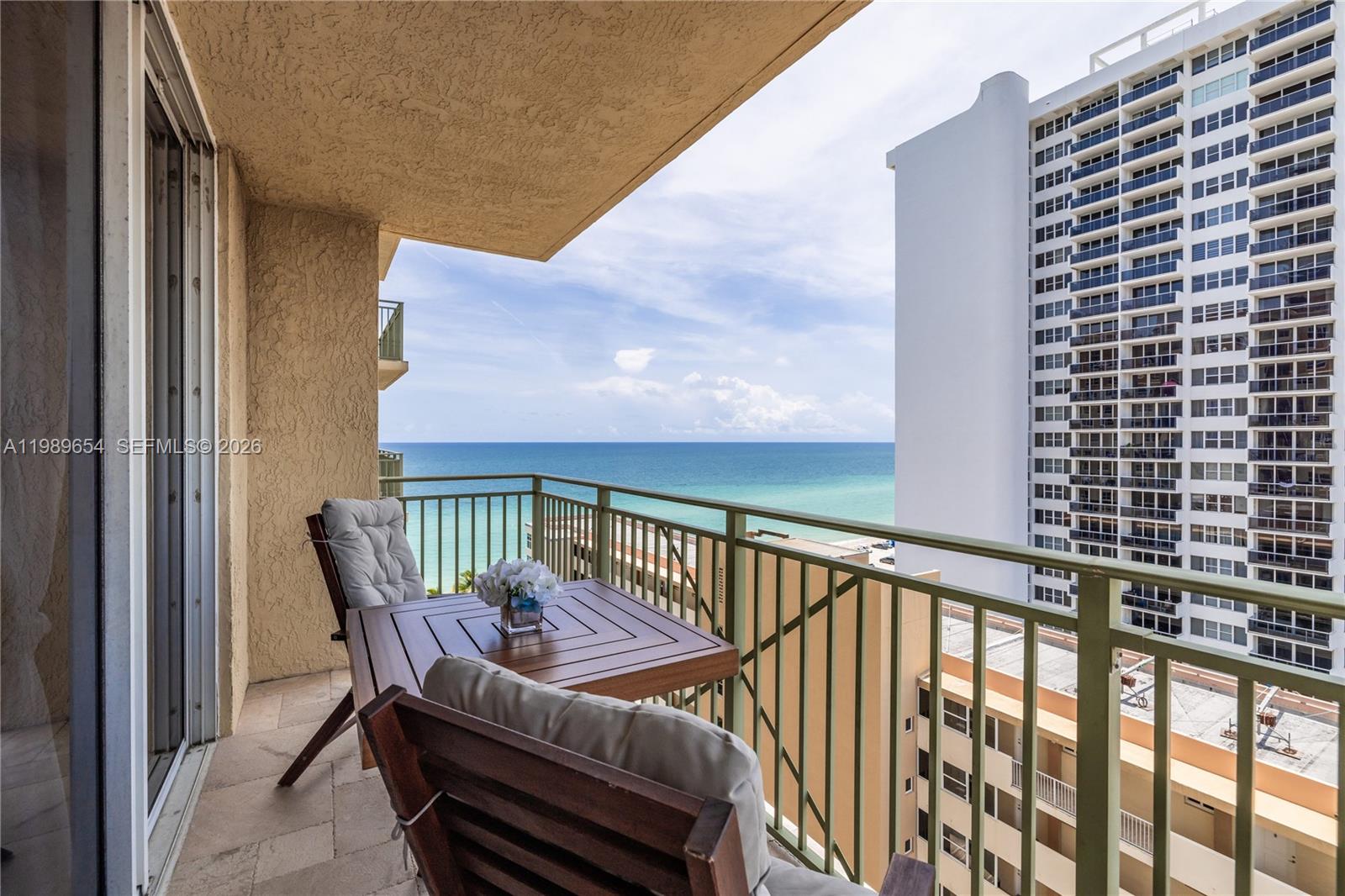 A balcony with a table and chairs overlooks the ocean and a neighboring high-rise building — 2080 S Ocean Dr, Hallandale Beach FL 33009, HALLANDALE BEACH, FL