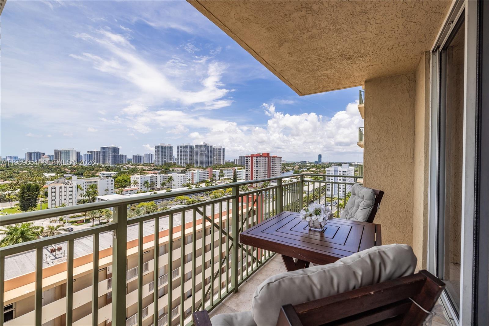 A balcony with a wooden table and chairs overlooks a city skyline and buildings — 2080 S Ocean Dr, Hallandale Beach FL 33009, HALLANDALE BEACH, FL