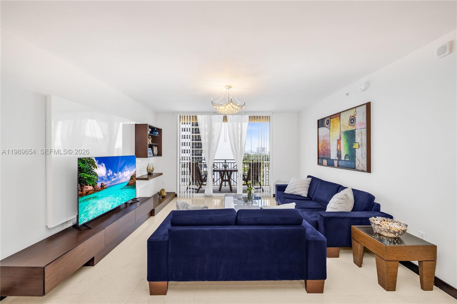A living room features a blue sectional sofa, a large television, and a balcony view — 2080 S Ocean Dr, Hallandale Beach FL 33009, HALLANDALE BEACH, FL