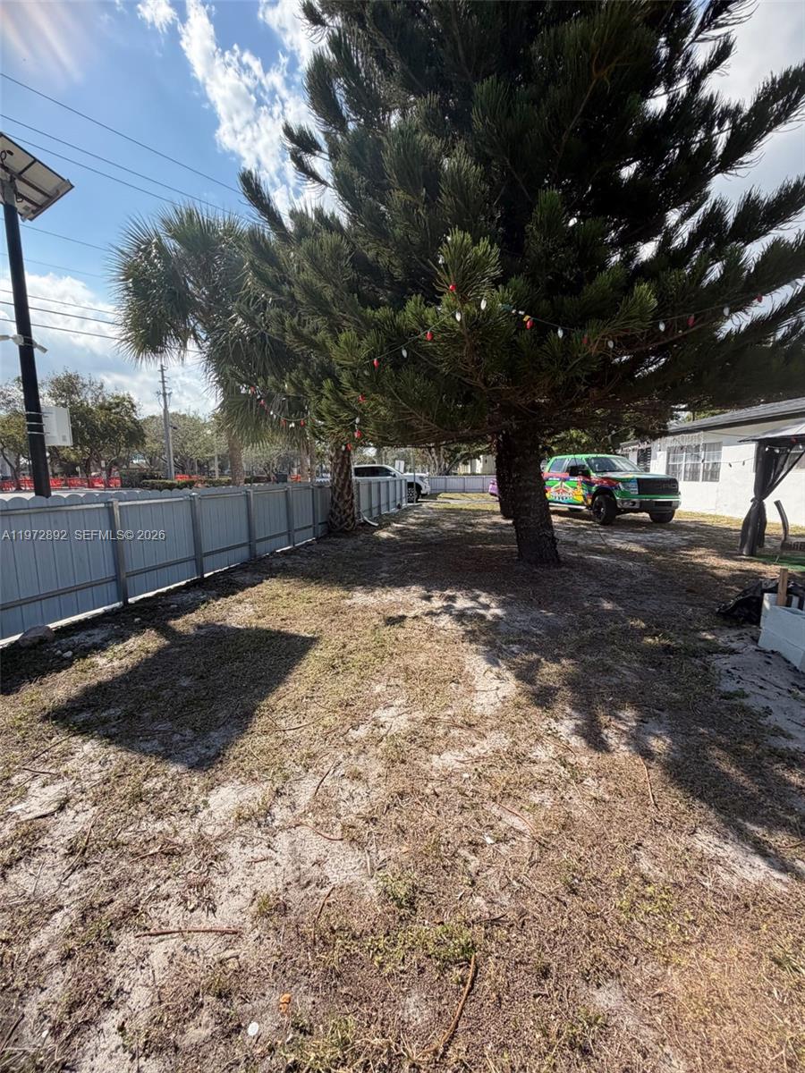 A large pine tree stands in a sandy yard enclosed by a gray fence — 331 NW 39th Ave # 1, Lauderhill FL 33311, LAUDERHILL, FL