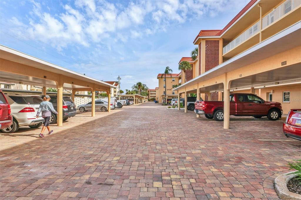 A paved parking area with covered spaces sits between two multi-story apartment buildings — 1250 N PORTOFINO DRIVE UNIT 303, SARASOTA, FL