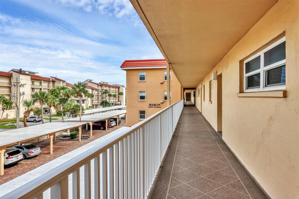 An exterior walkway overlooks a parking lot with covered carports and adjacent apartment buildings — 1250 N PORTOFINO DRIVE UNIT 303, SARASOTA, FL
