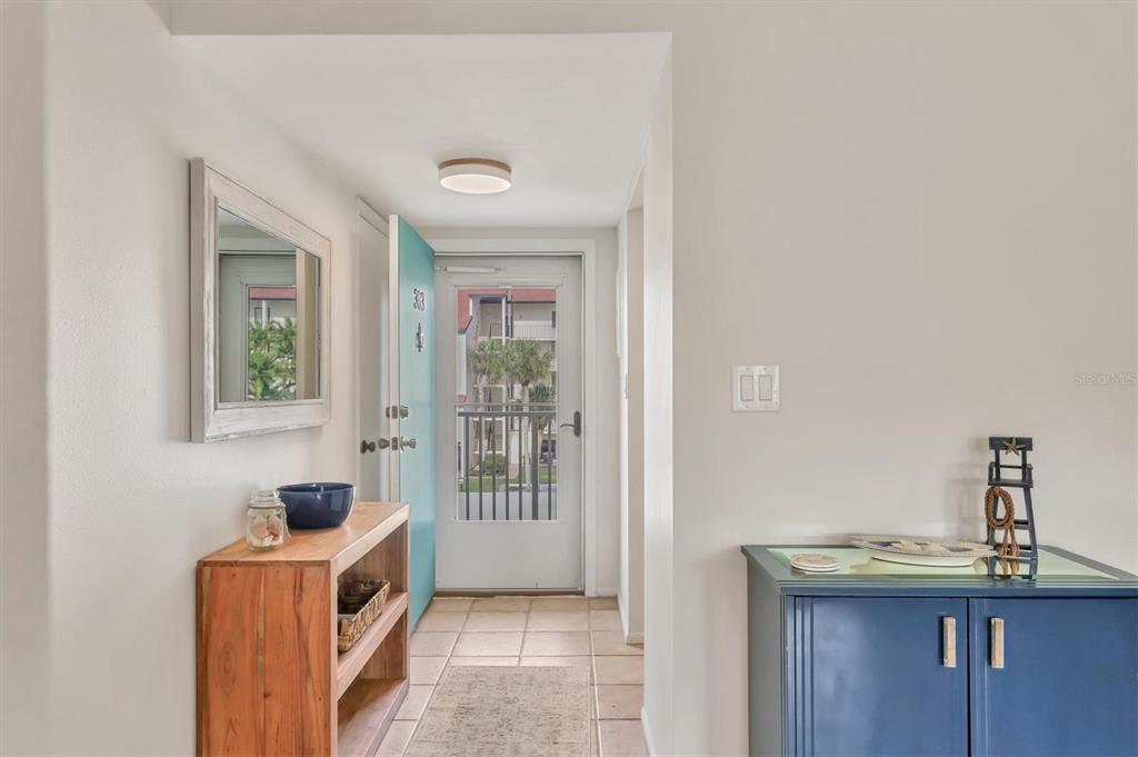 An entryway features a light blue door, tiled floors, a wooden console table, and a mirror — 1250 N PORTOFINO DRIVE UNIT 303, SARASOTA, FL