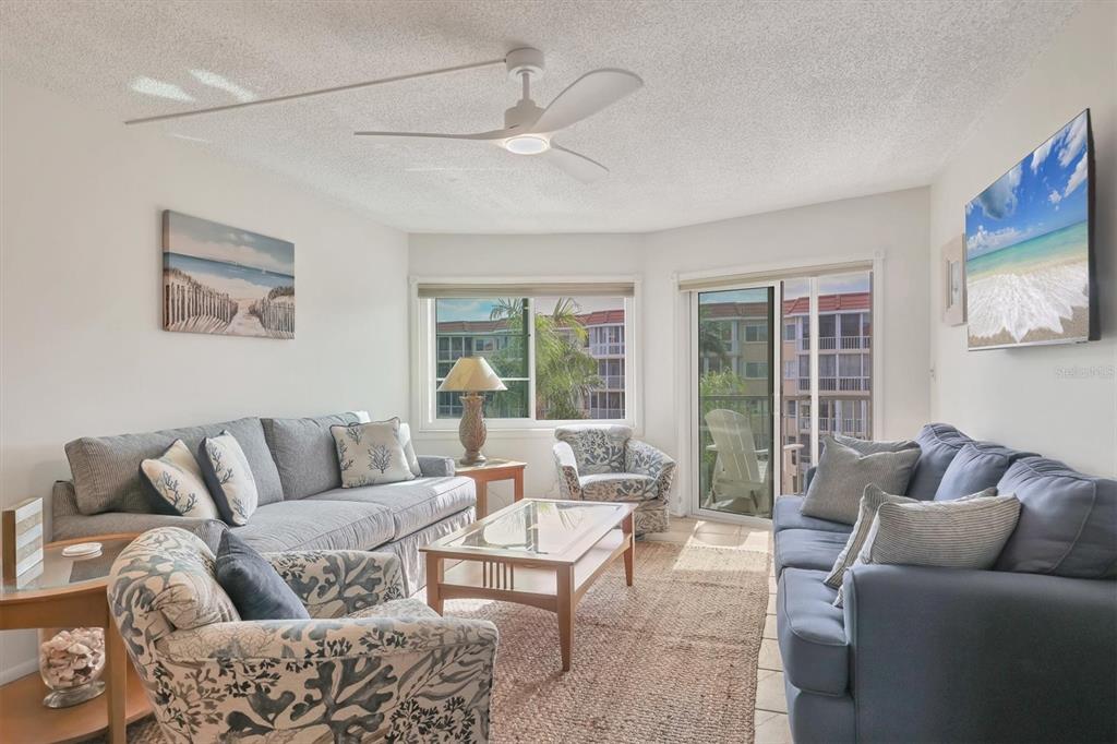 A living room features two sofas, two patterned armchairs, a coffee table, and a ceiling fan — 1250 N PORTOFINO DRIVE UNIT 303, SARASOTA, FL