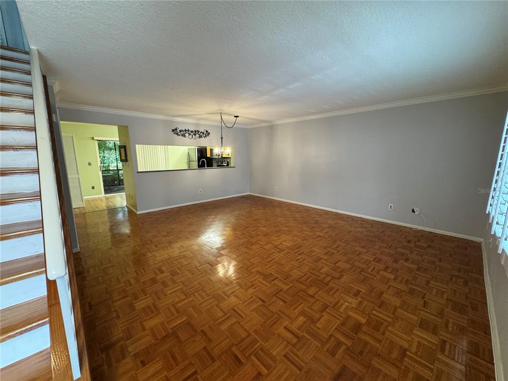 A living room with parquet wood flooring, a staircase, and a pass-through to the kitchen — 705 BOUGH AVENUE, CLEARWATER, FL