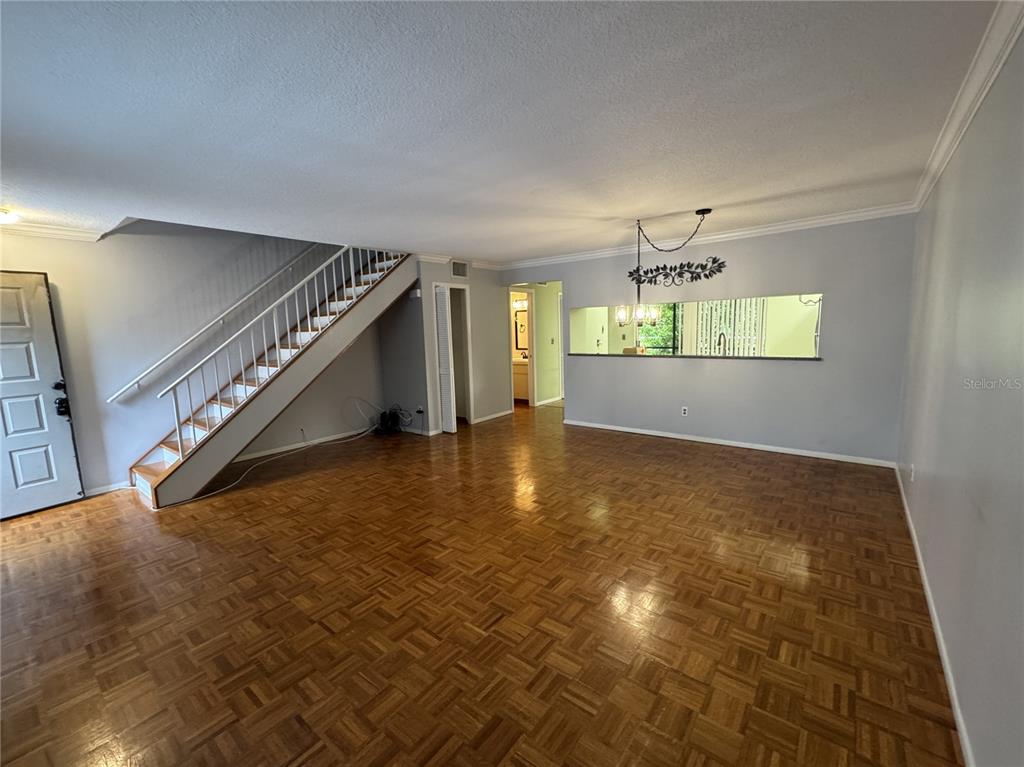 An open living area features parquet wood flooring, a staircase, and a kitchen pass-through window — 705 BOUGH AVENUE, CLEARWATER, FL