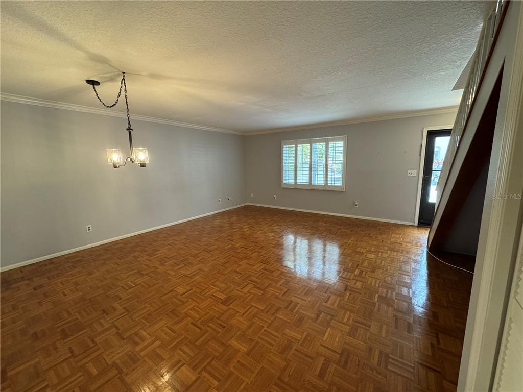 An empty room features parquet wood flooring, light gray walls, and a hanging light fixture — 705 BOUGH AVENUE, CLEARWATER, FL