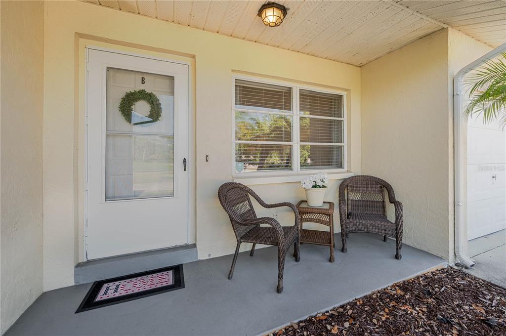 A covered front porch features a white door, two wicker chairs, and a small table — 182 BOUNDARY BOULEVARD UNIT B, ROTONDA WEST, FL