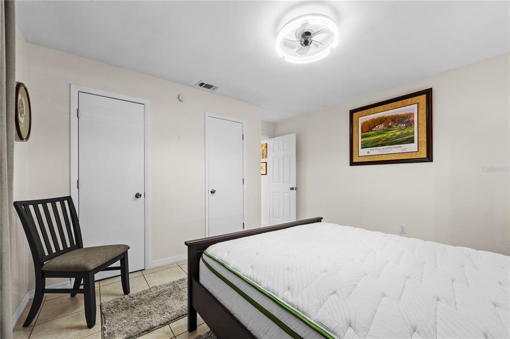 A bedroom features a bed, a chair, tiled floors, and a ceiling fan light fixture — 182 BOUNDARY BOULEVARD UNIT B, ROTONDA WEST, FL