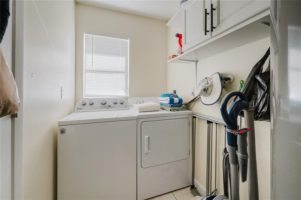 A laundry room features a white washer and dryer, upper cabinets, and a window — 182 BOUNDARY BOULEVARD UNIT B, ROTONDA WEST, FL