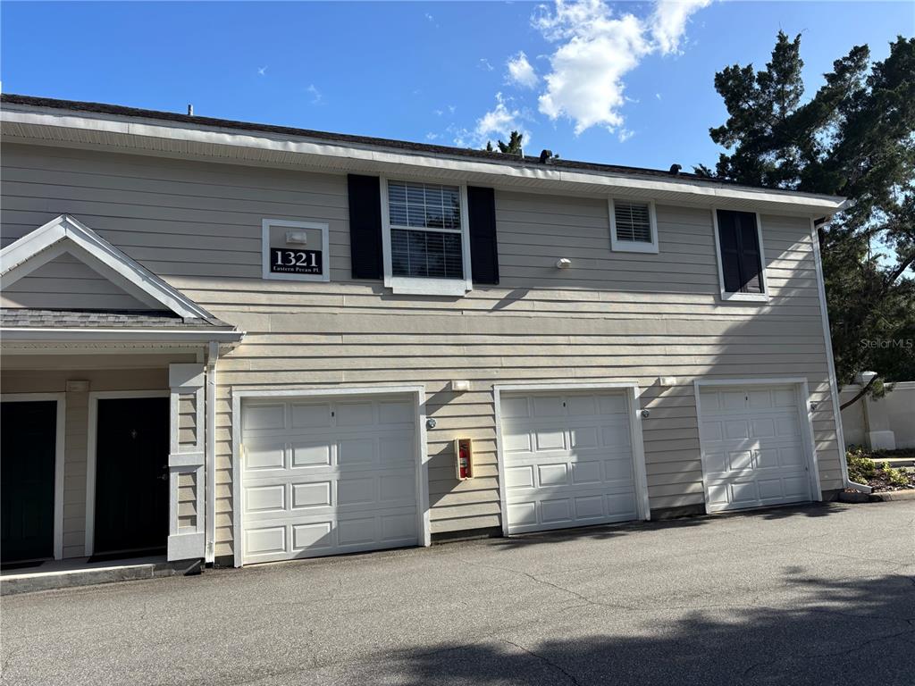 A two-story building exterior features beige horizontal siding, three white garage doors, and a doorway — 1321 EASTERN PECAN PLACE UNIT 201, WINTER GARDEN, FL