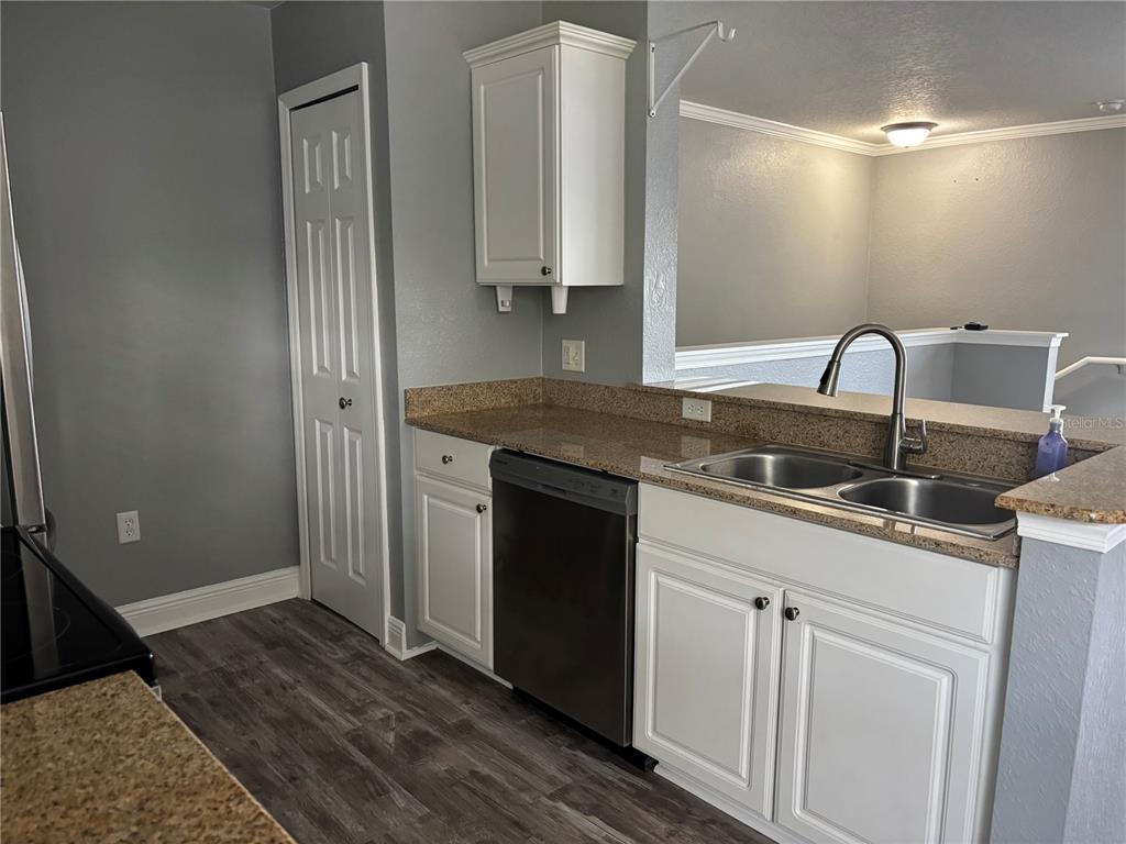 A kitchen features white cabinets, granite countertops, a stainless steel dishwasher, and gray flooring — 1321 EASTERN PECAN PLACE UNIT 201, WINTER GARDEN, FL