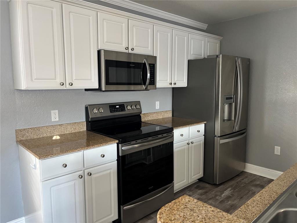 A kitchen features white cabinets, granite countertops, and stainless steel appliances against gray walls — 1321 EASTERN PECAN PLACE UNIT 201, WINTER GARDEN, FL